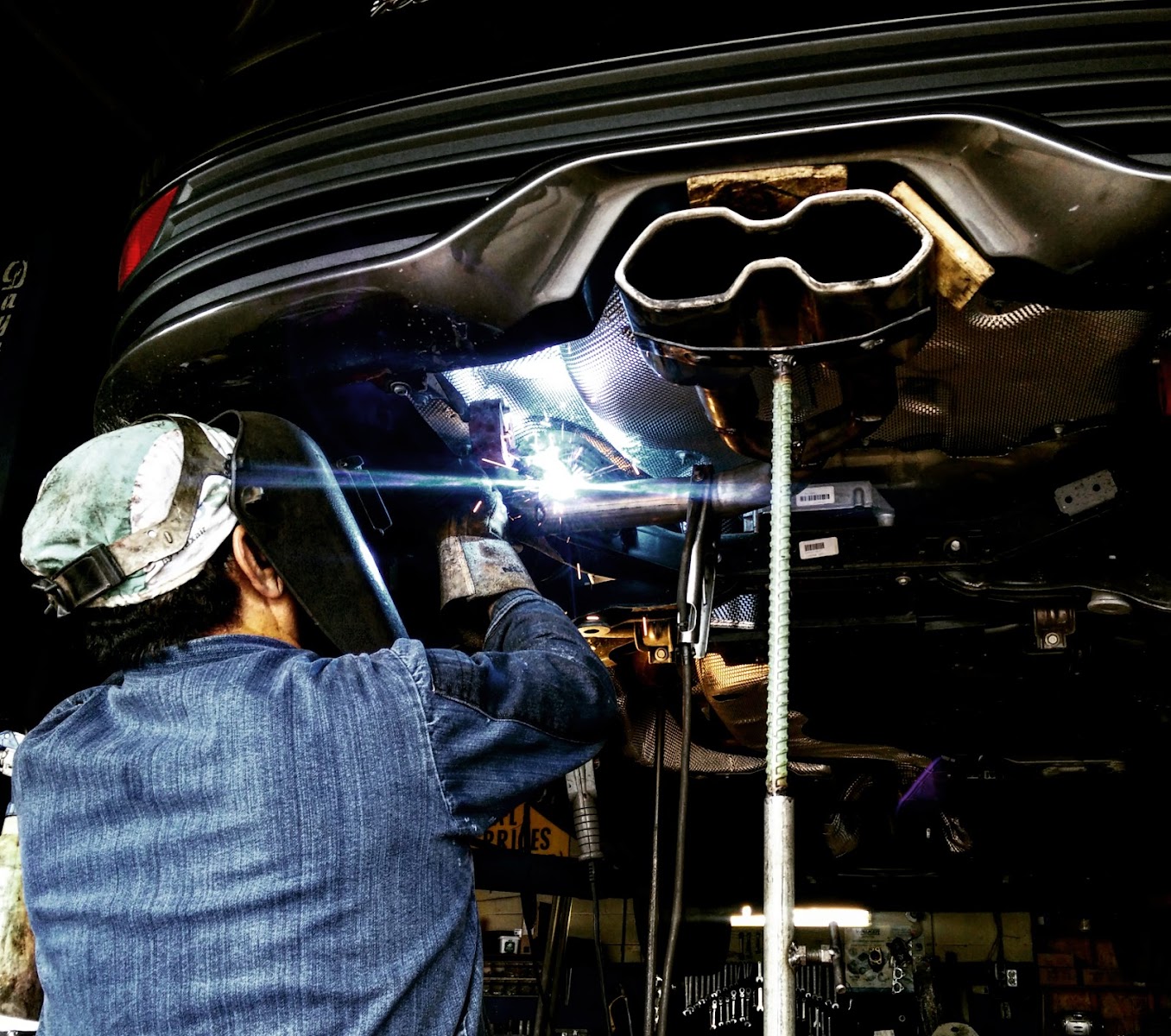 A mechanic welding under the rear of a car at Asad Mufflers.